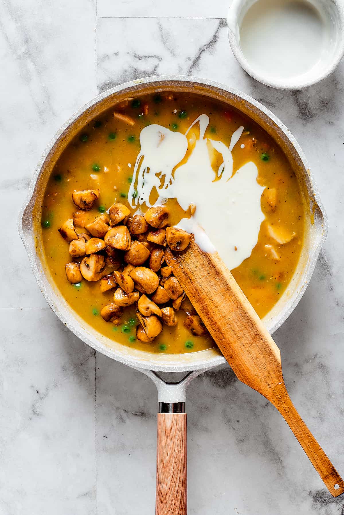 A wooden spoon stirs heavy cream into a pot of Turkey a La King.