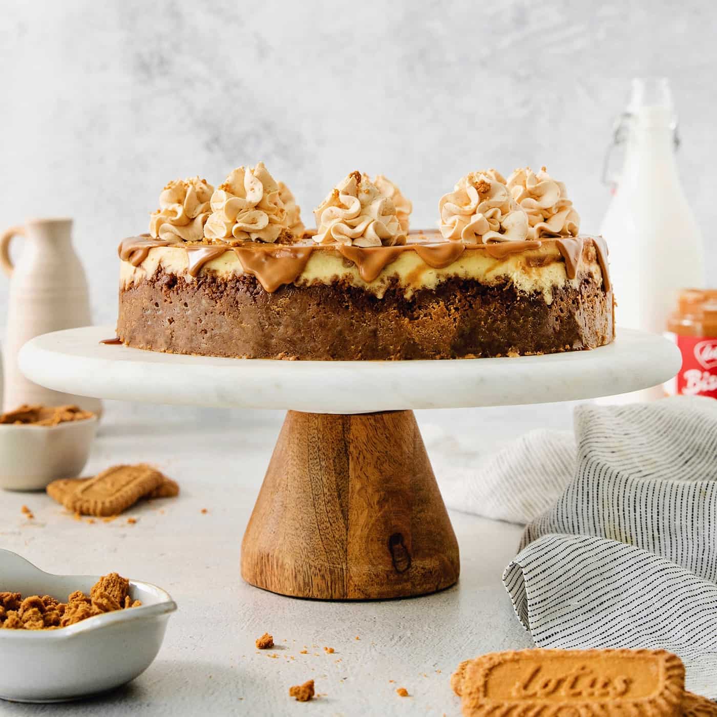 A biscoff cheesecake topped with butterscotch whipped cream is shown on a cake stand.