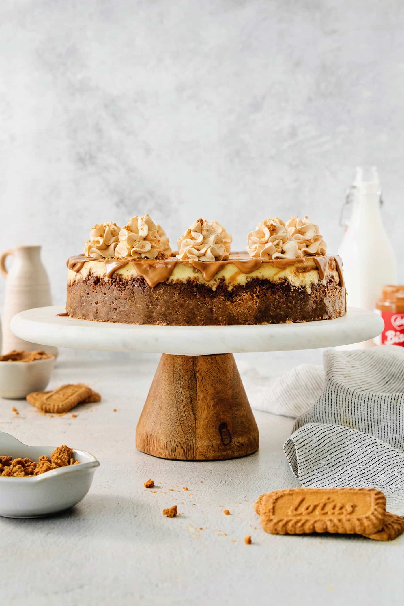 A biscoff cheesecake topped with butterscotch whipped cream is shown on a cake stand.