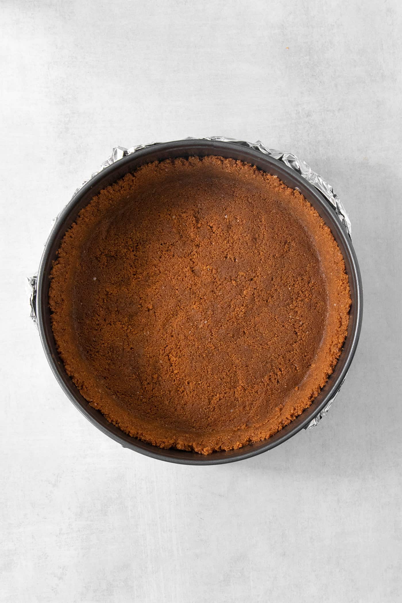 A biscoff cookie crust is shown in a springform pan.
