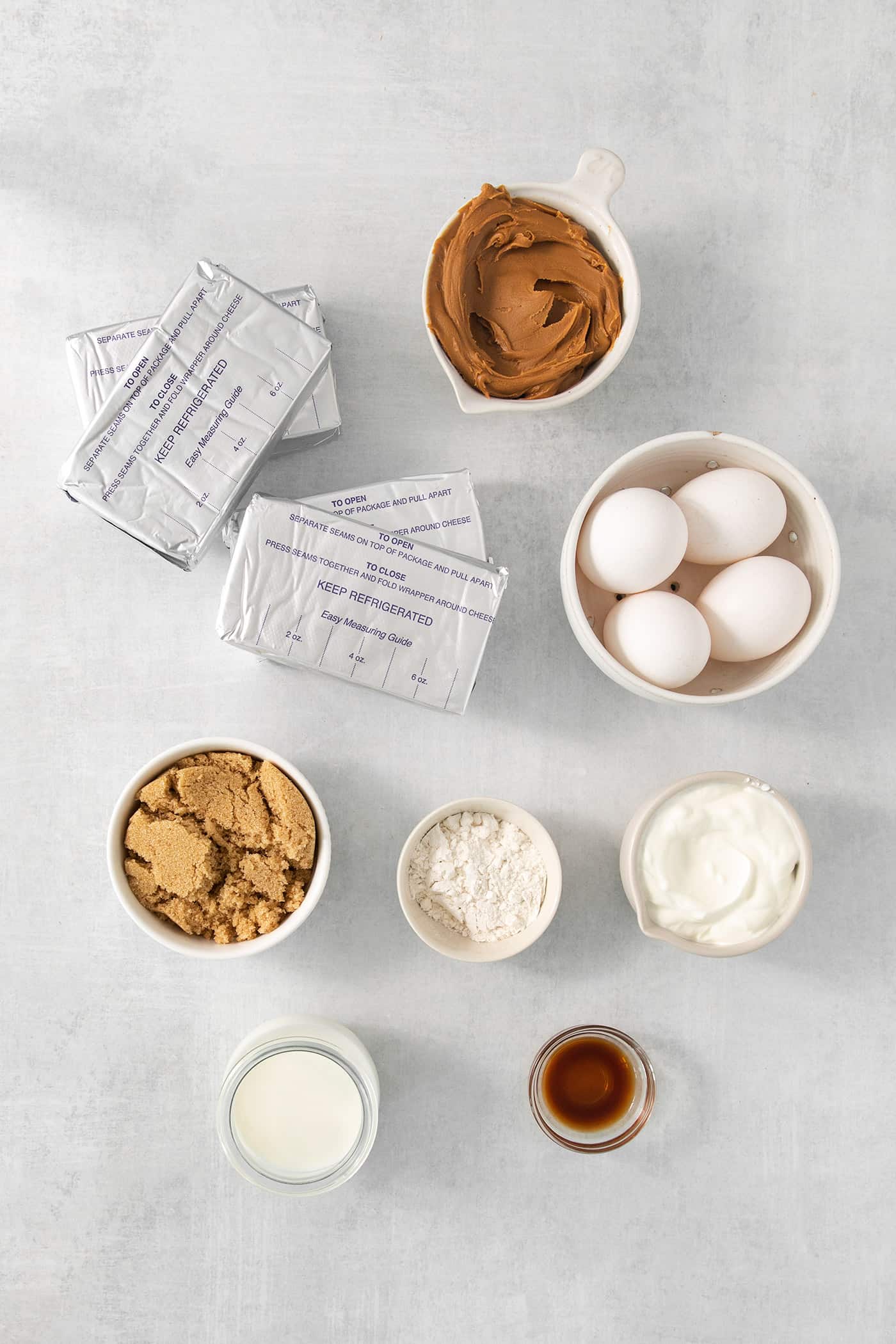 Ingredients needed to make biscoff cheesecake are shown on a white background: cream cheese, eggs, cookie butter, vanilla, sugar, cookies.