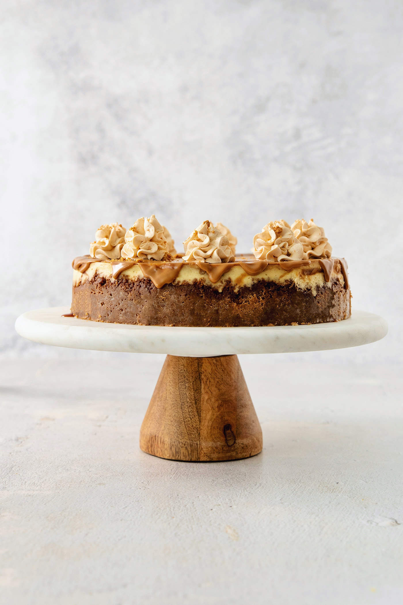 A biscoff cheesecake topped with butterscotch whipped cream is shown on a cake stand.
