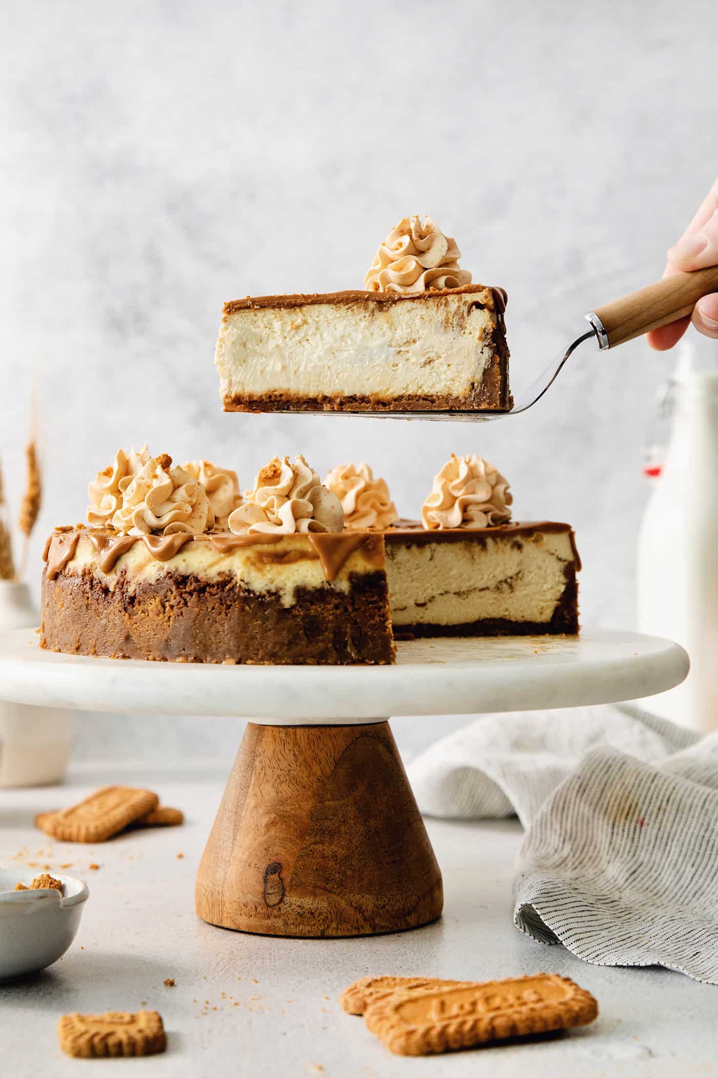 A biscoff cheesecake topped with butterscotch whipped cream is shown on a cake stand.