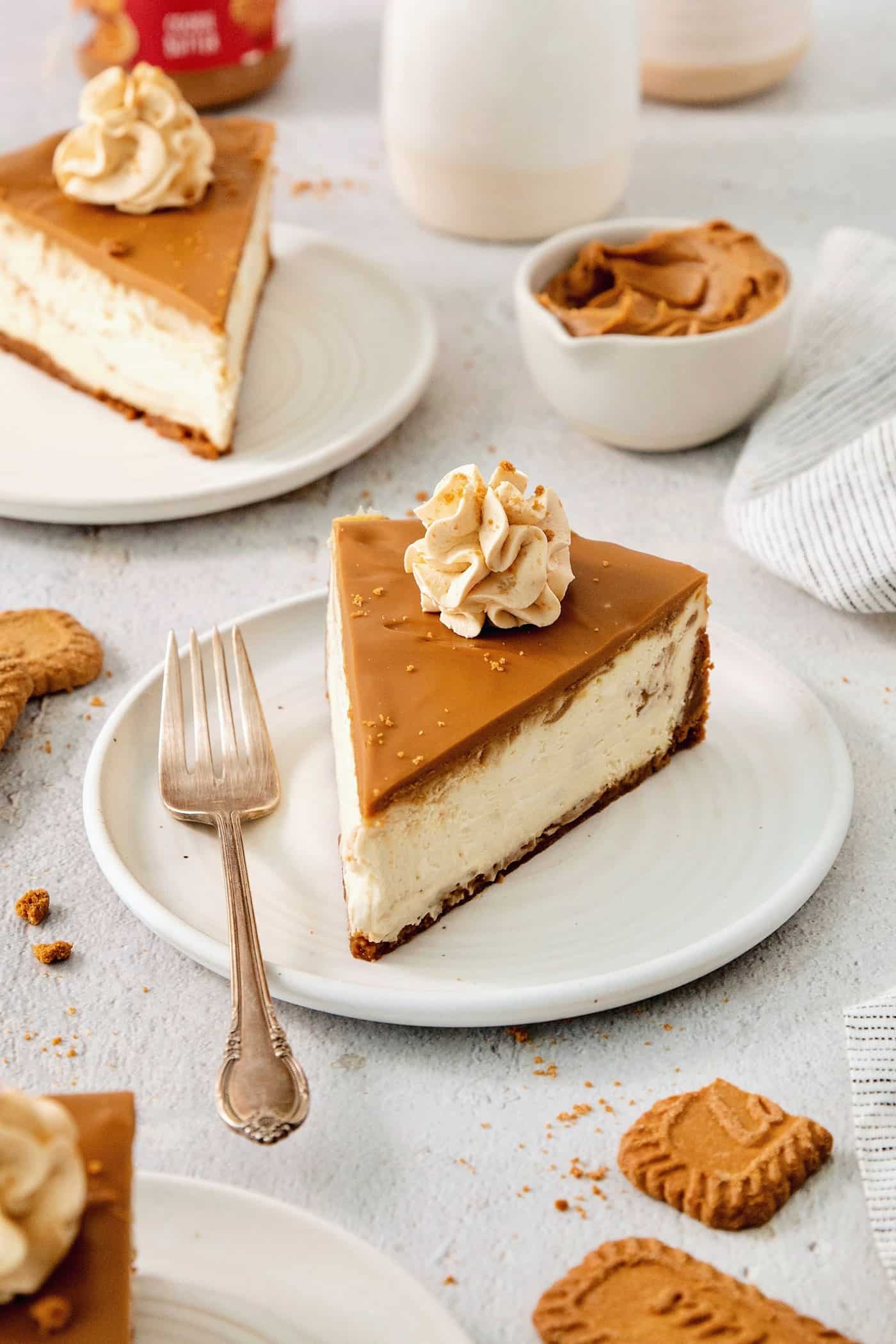 A slice of biscoff cheesecake is shown on a plate with biscoff cookie butter in the background.