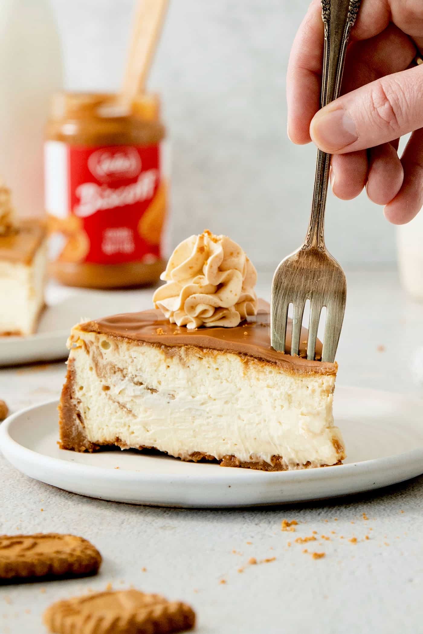 A fork cuts into a slice of biscoff cheesecake on a white plate.