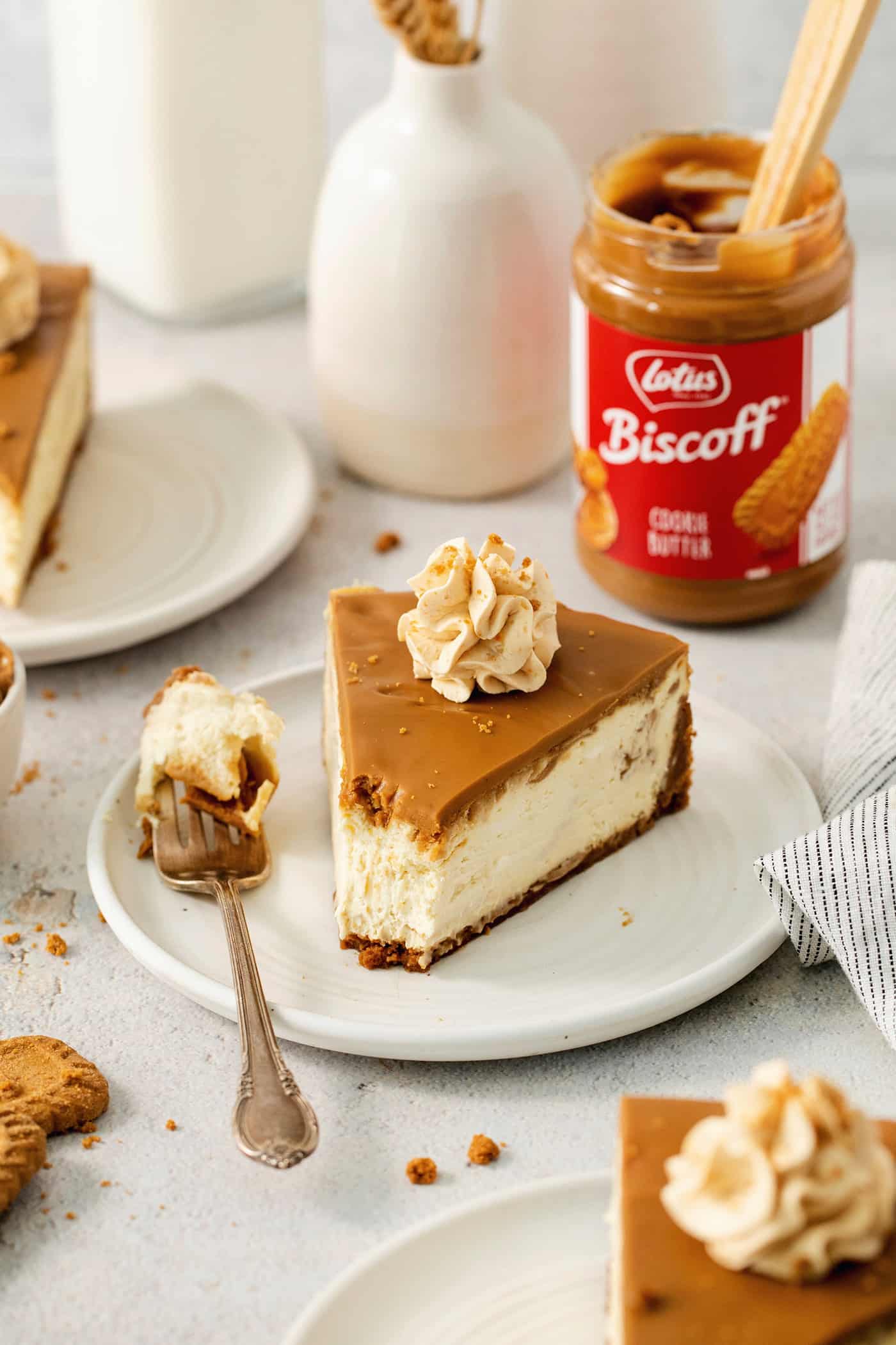 A slice of biscoff cheesecake is shown on a plate with biscoff cookie butter in the background.