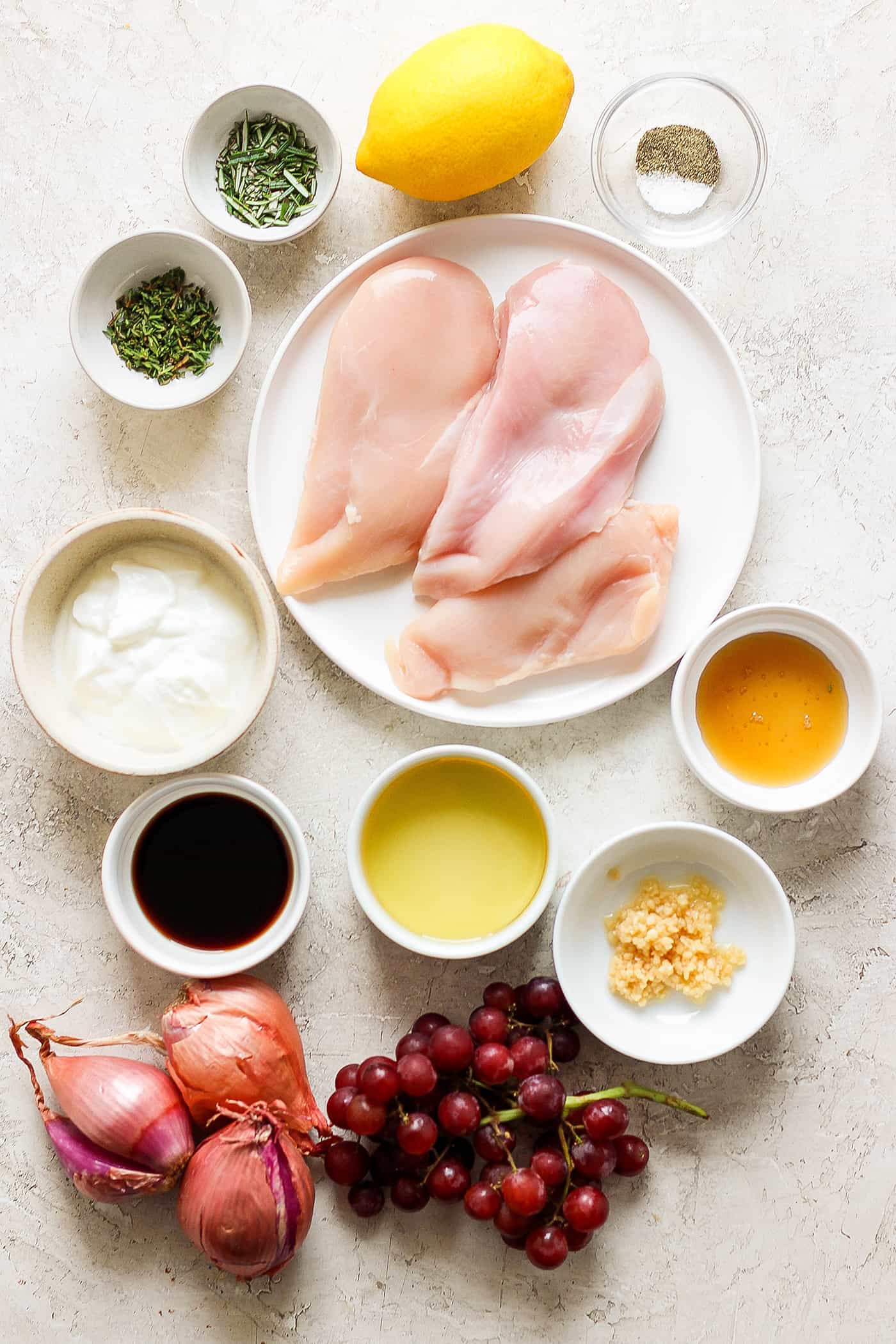 The ingredients for chicken kabobs are shown: chicken, yogurt, lemon juice and zest, olive oil, shallots, vinegar, and grapes.