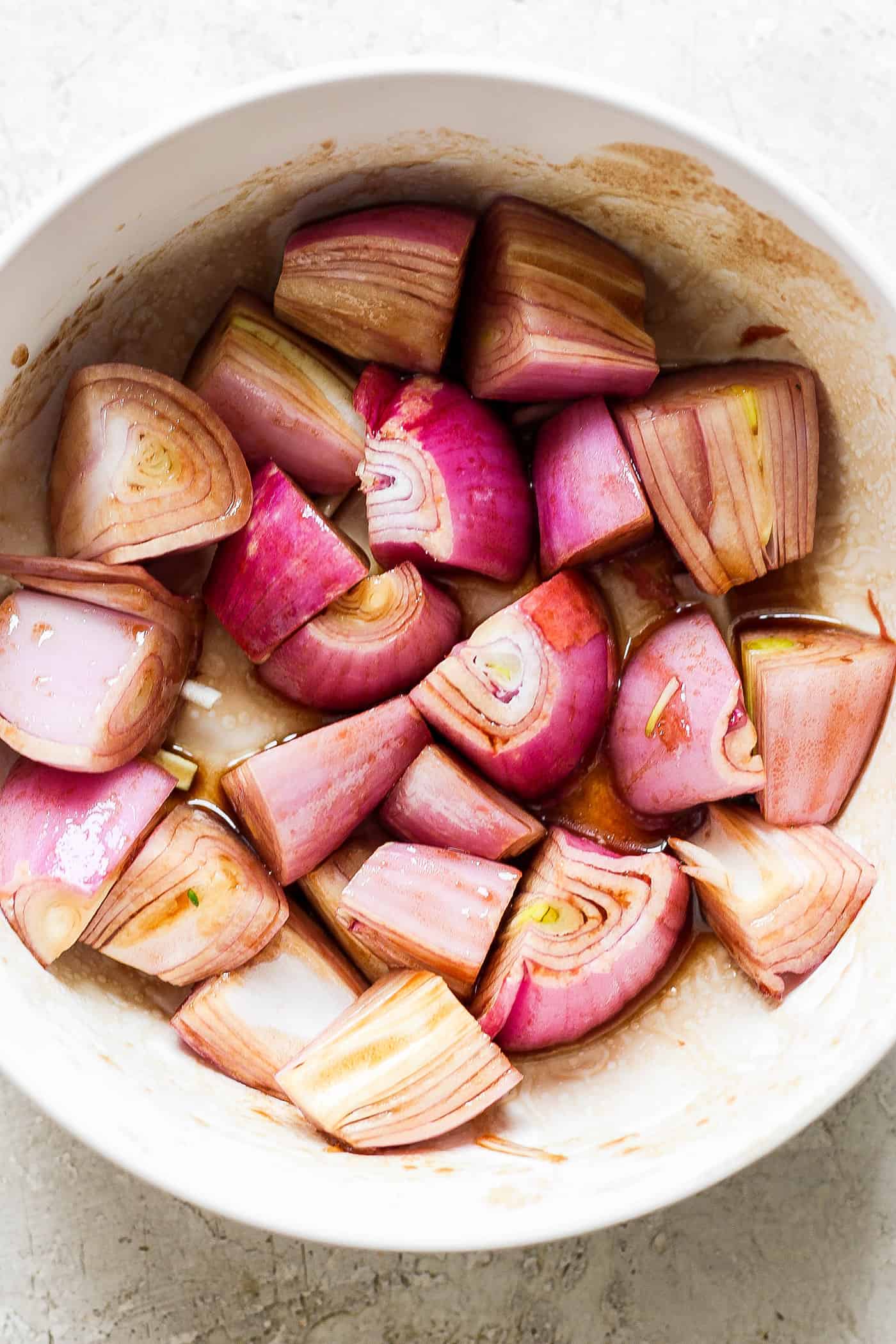 Shallots are shown marinating in a white bowl.