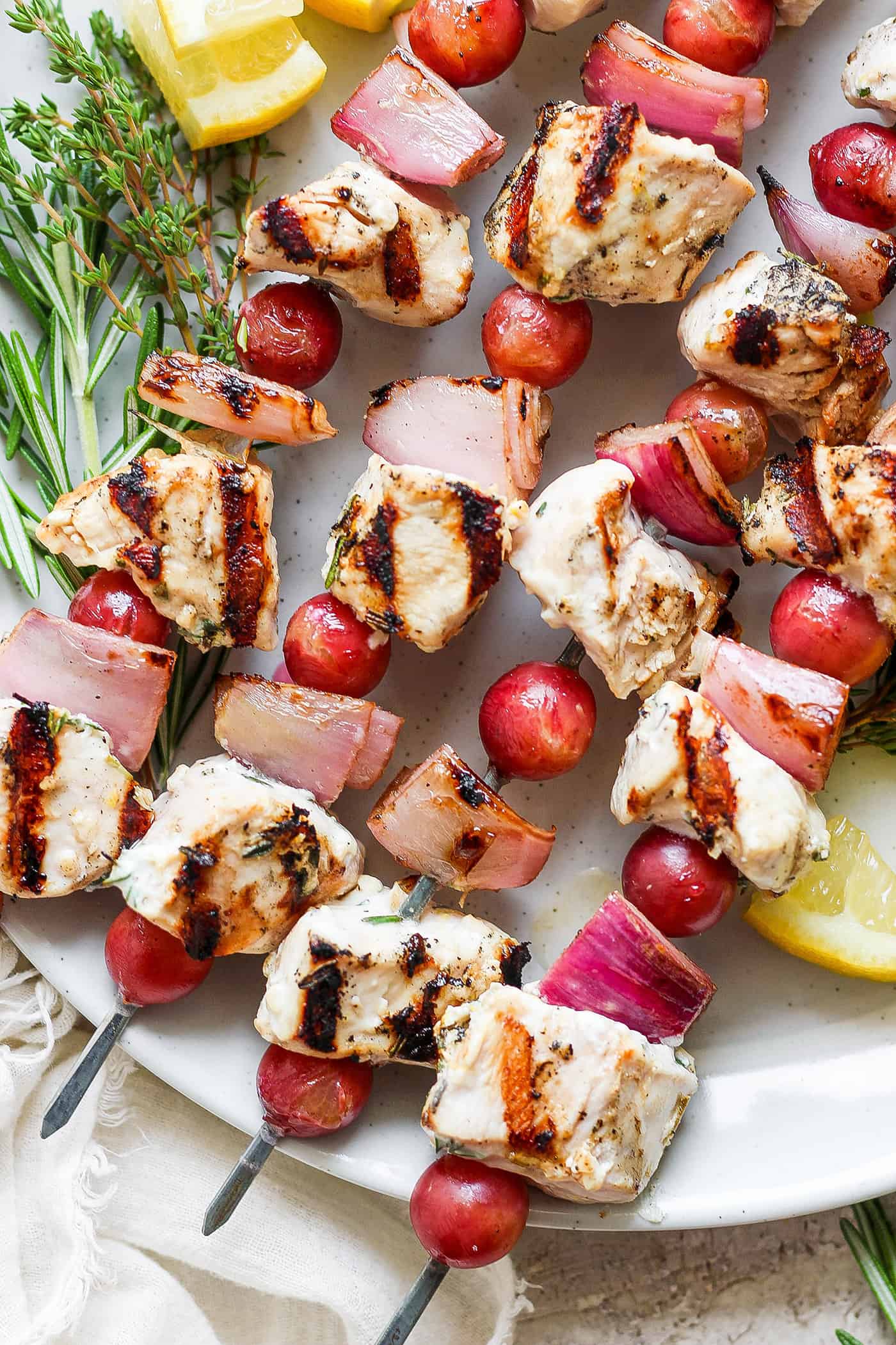 A white plate holds chicken kabobs with grapes on skewers.