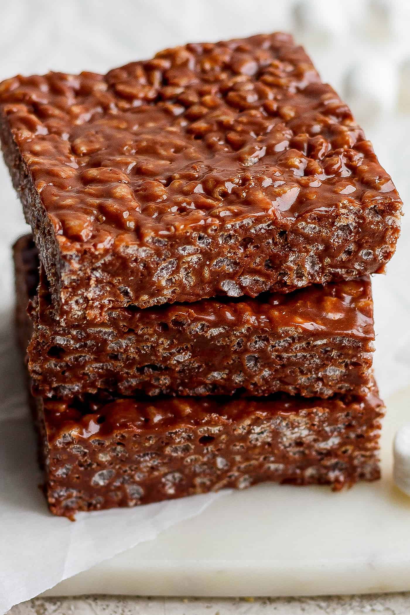 A stack of 3 chocolate rice krispie treats on a white board.