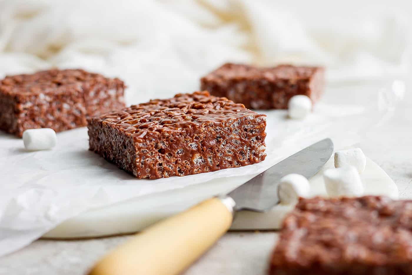 Chocolate rice krispie treats are shown on a white cutting board.