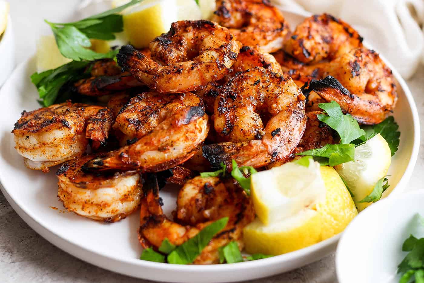 A close up of a platter of grilled shrimp and lemon wedges.