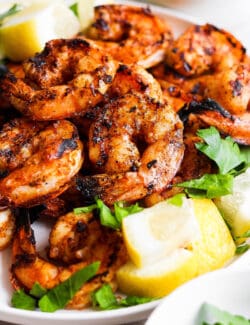 A close up of a platter of grilled shrimp and lemon wedges.