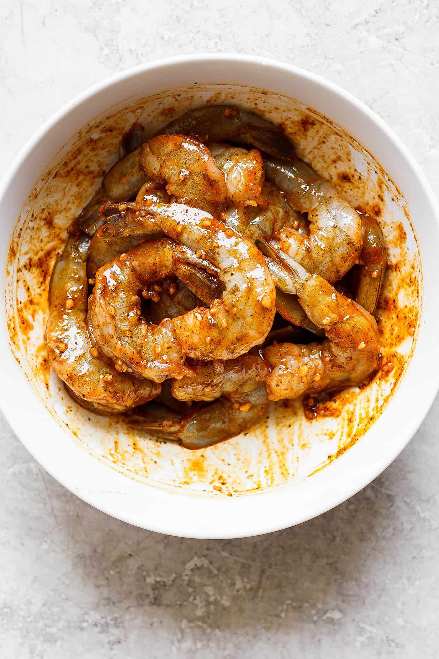 A white bowl of shrimp in a spicy marinade.