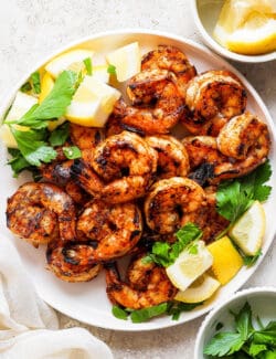 A platter of grilled shrimp surrounded by lemon wedges.