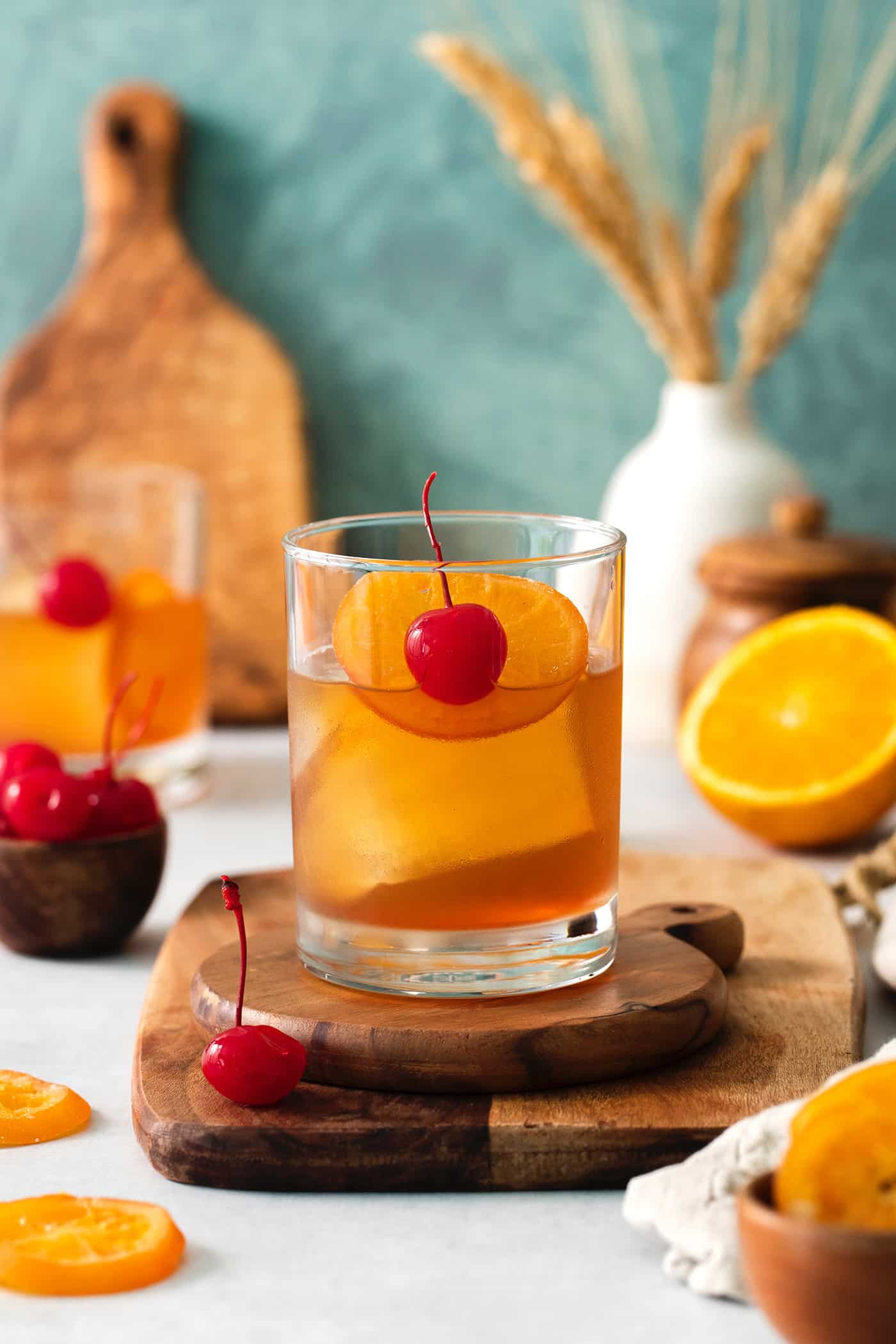 An old fashioned drink is shown on a wood board with more drinks and oranges in the background.