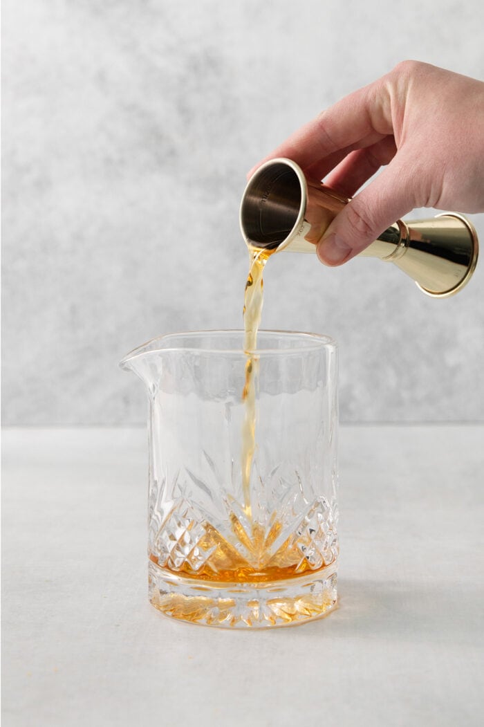 A hand holds a cocktail measure and pours bourbon into a glass of old fashioned.