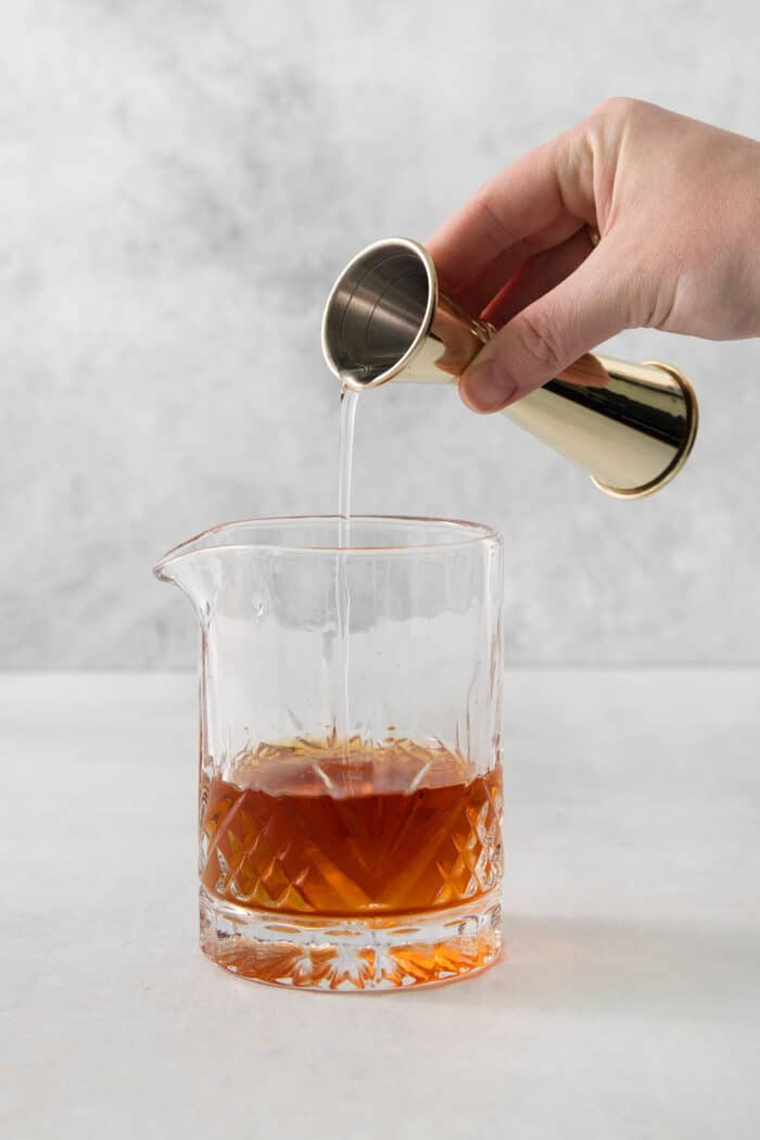 A hand holds a cocktail measure and pours simple syrup into a glass of old fashioned.