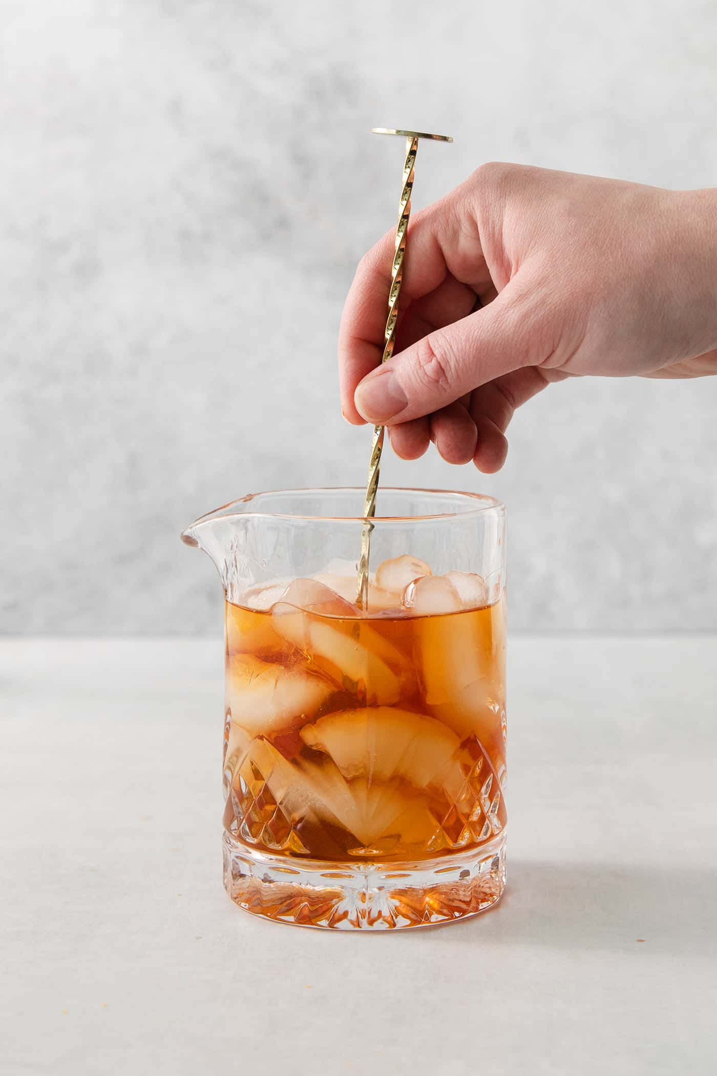 A hand holds a stirrer and stirs a glass of old fashioned.