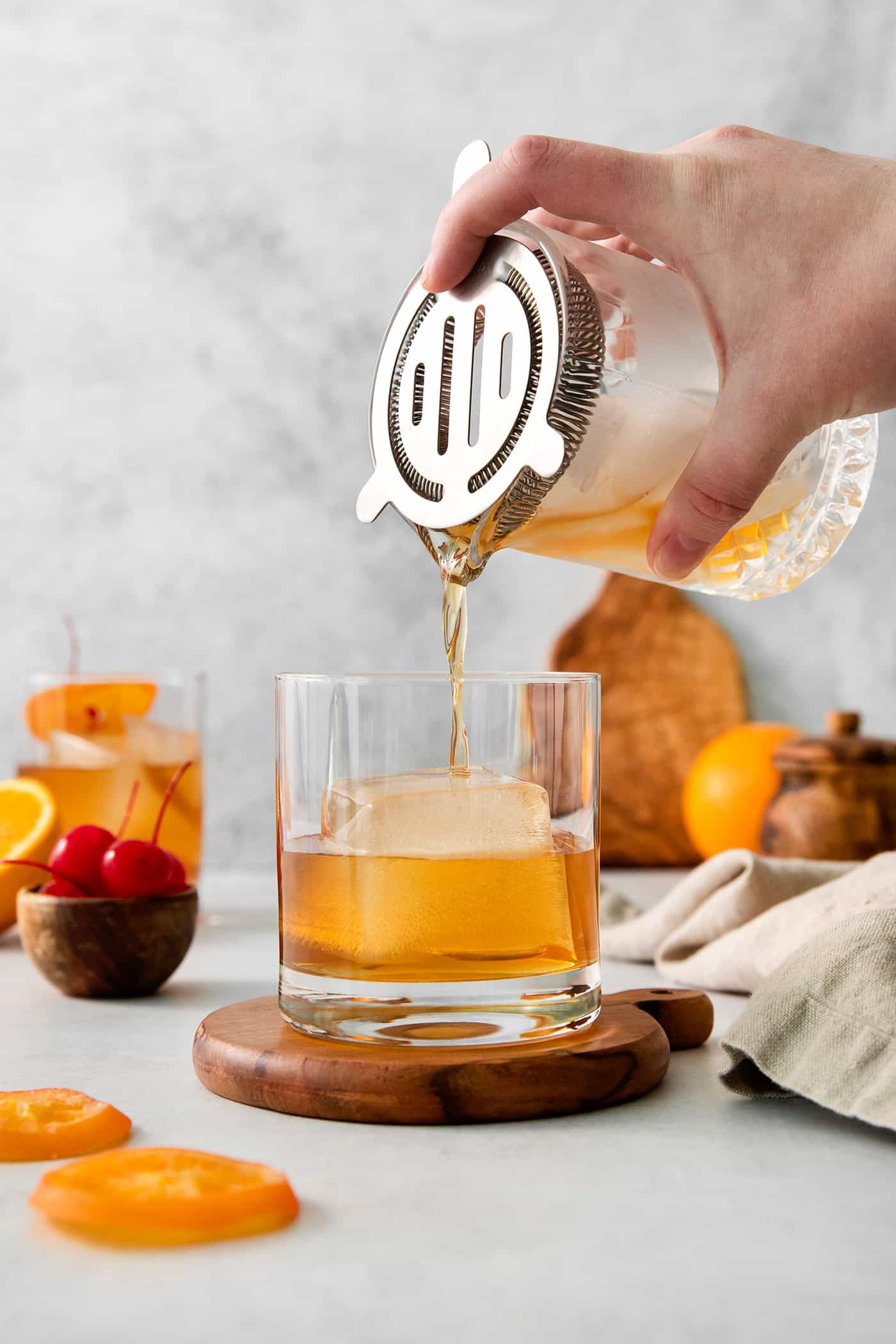 A hand holds a cocktail shaker and pours an old fashioned drink into a glass.