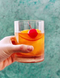 a hand holding a glass of an Old Fashioned cocktail