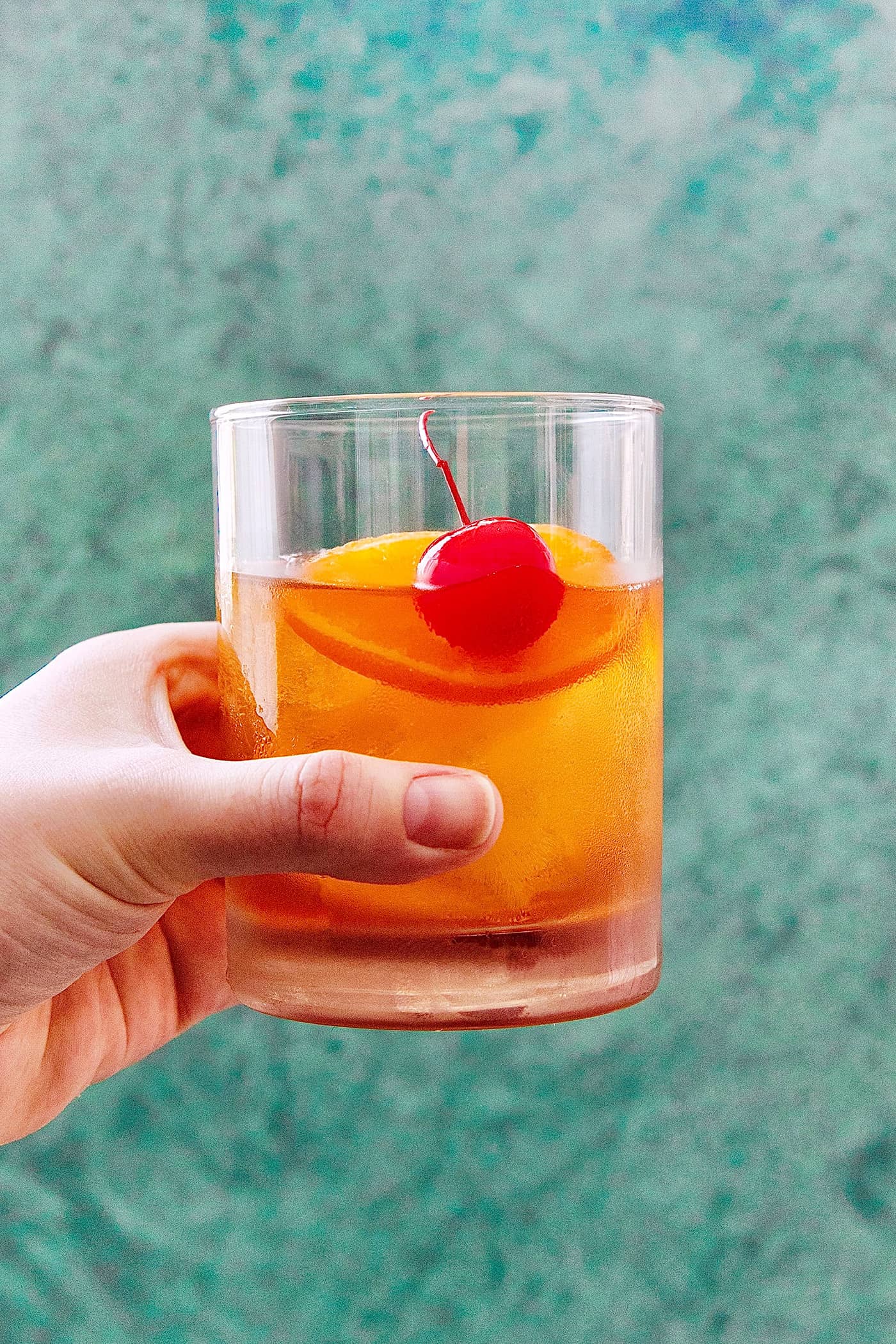 a hand holding a glass of an Old Fashioned cocktail