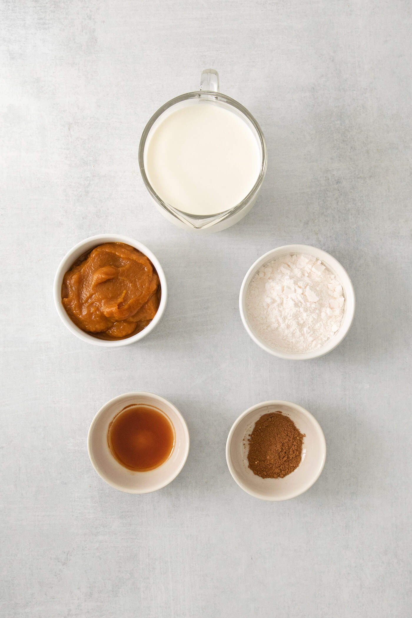 Ingredients for the pumpkin layer for pumpkin cheesecake bars are shown in bowls: pumpkin puree, spices, powdered sugar.