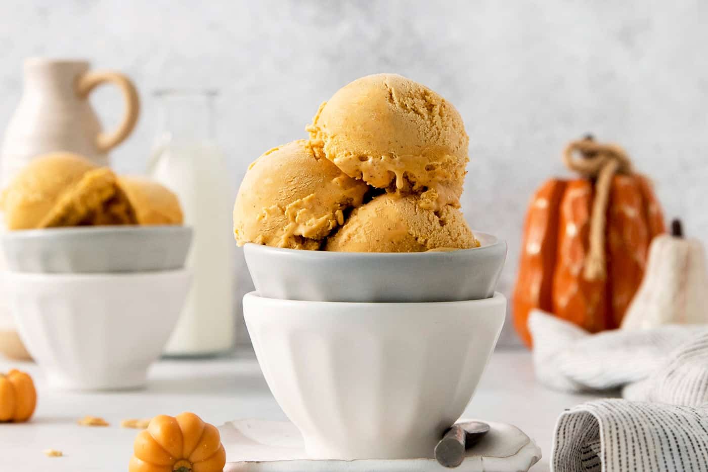 Three scoops of orange pumpkin ice cream are shown in a gray bowl stacked in a white bowl.