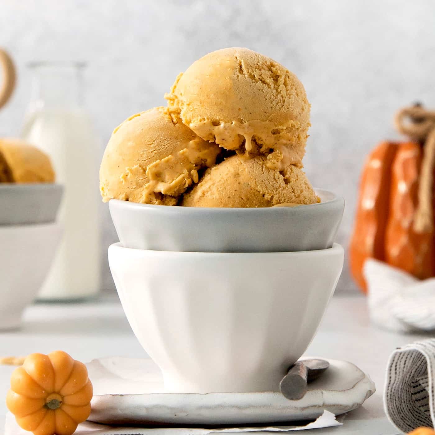 Three scoops of orange pumpkin ice cream are shown in a gray bowl stacked in a white bowl.