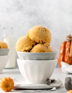 Three scoops of orange pumpkin ice cream are shown in a gray bowl stacked in a white bowl.