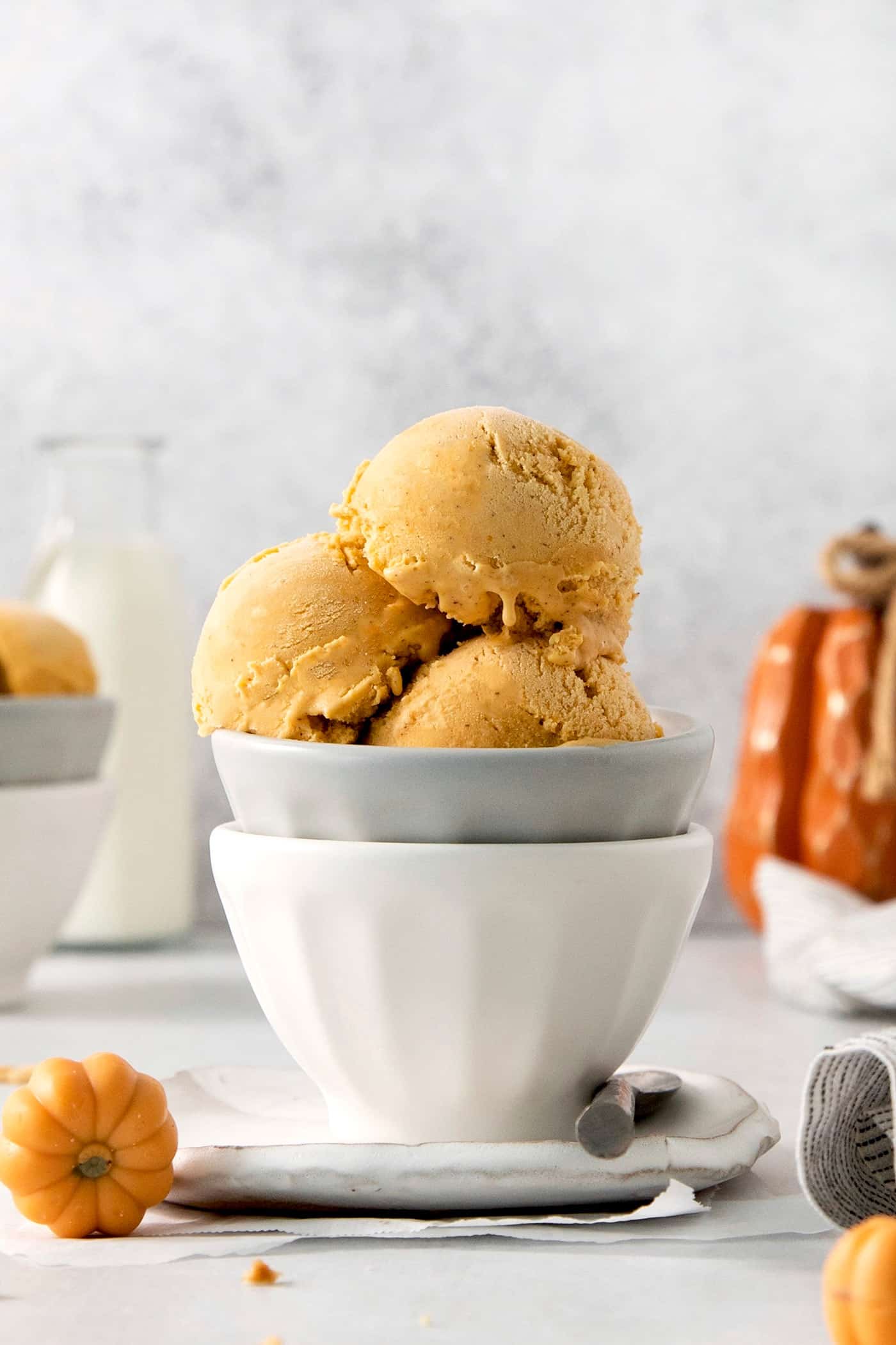 Three scoops of orange pumpkin ice cream are shown in a gray bowl stacked in a white bowl.