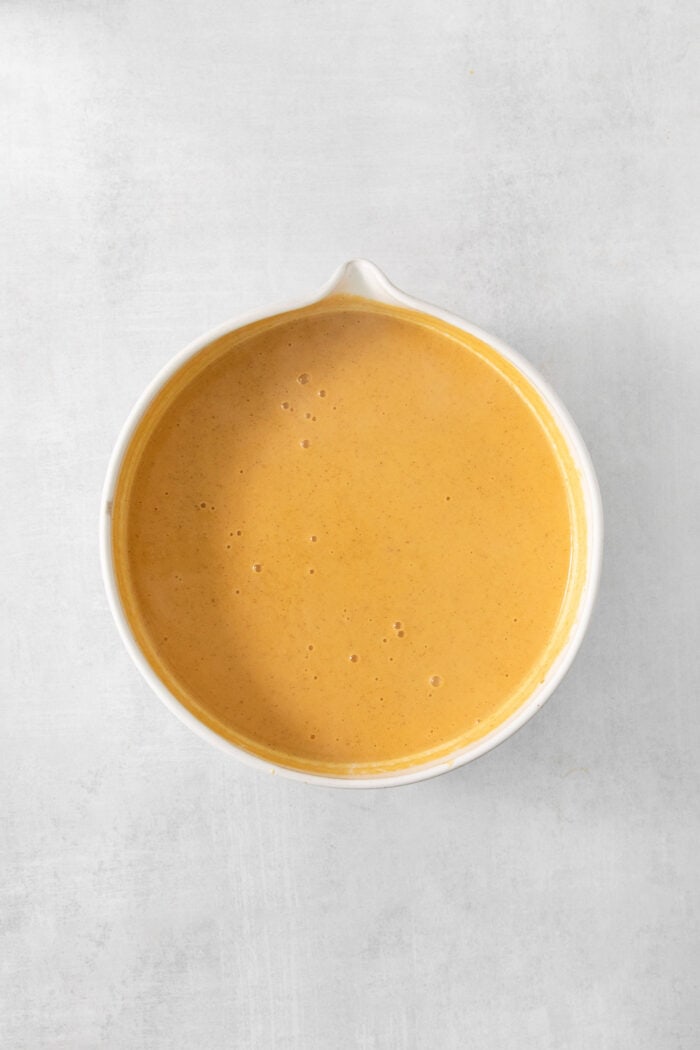 A white bowl of orange custard for pumpkin ice cream is shown on a white background.