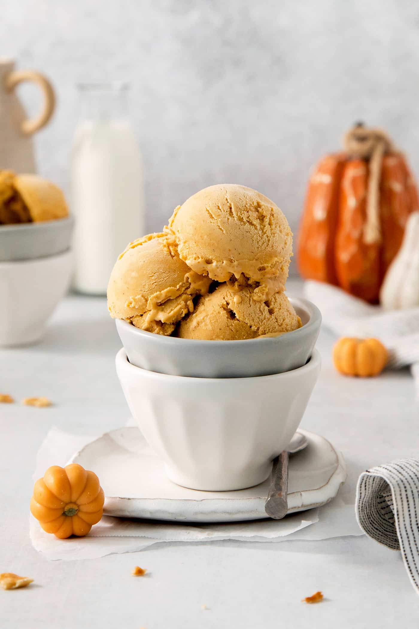 Three scoops of orange pumpkin ice cream are shown in a gray bowl stacked in a white bowl.