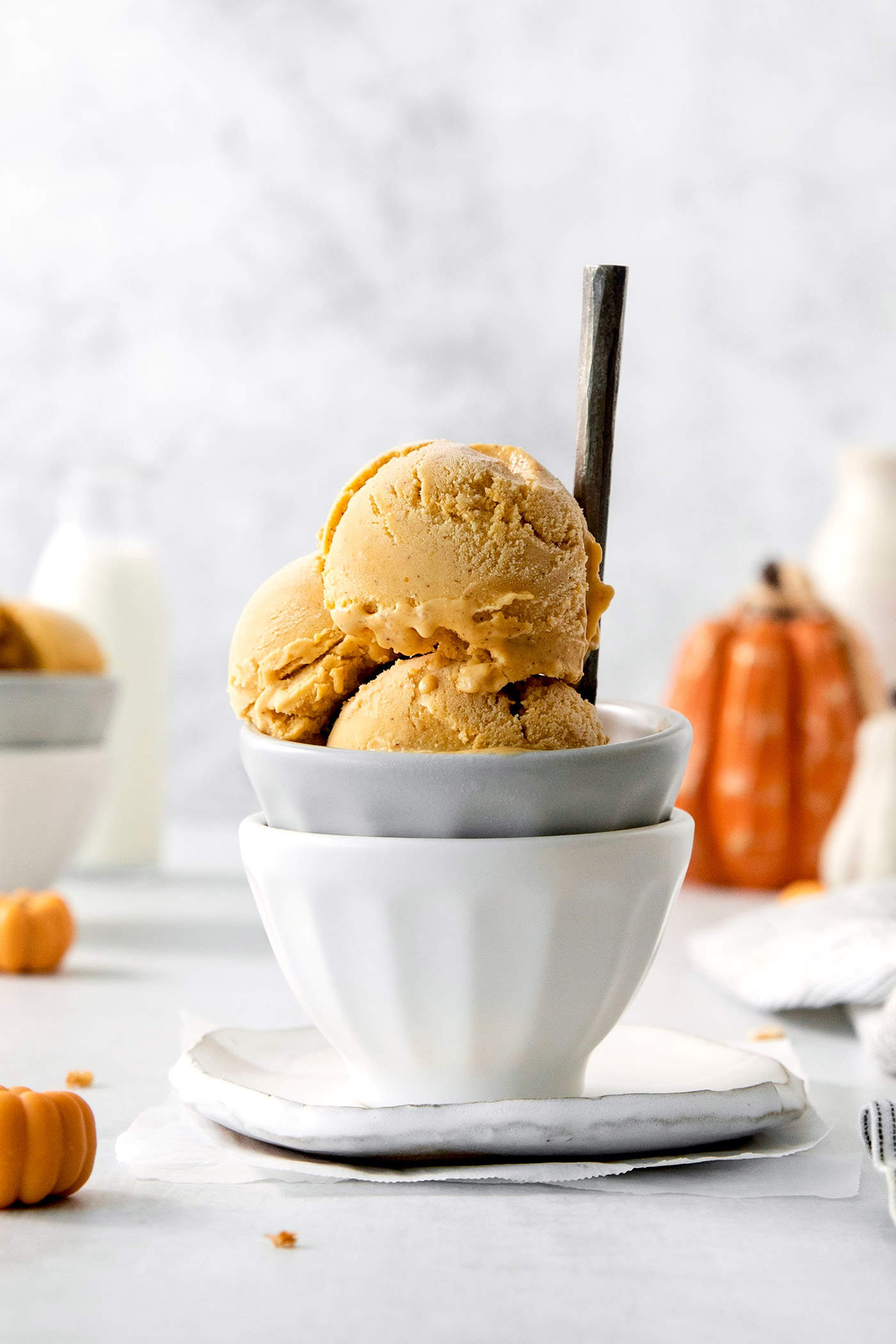 Three scoops of orange pumpkin ice cream are shown in a gray bowl stacked in a white bowl.