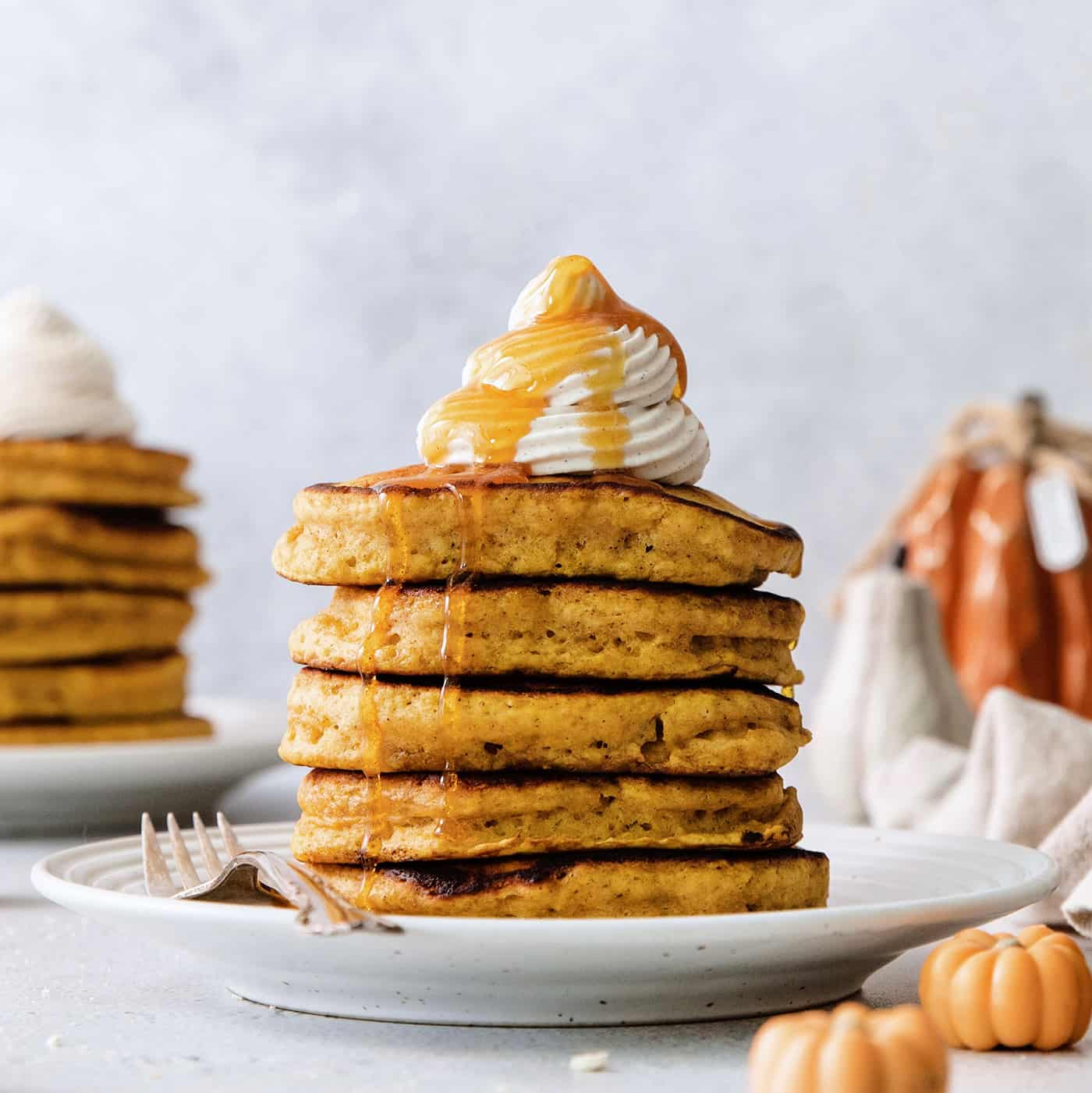 A stack of pumpkin pancakes topped with maple cinnamon whipped cream on a white plate.