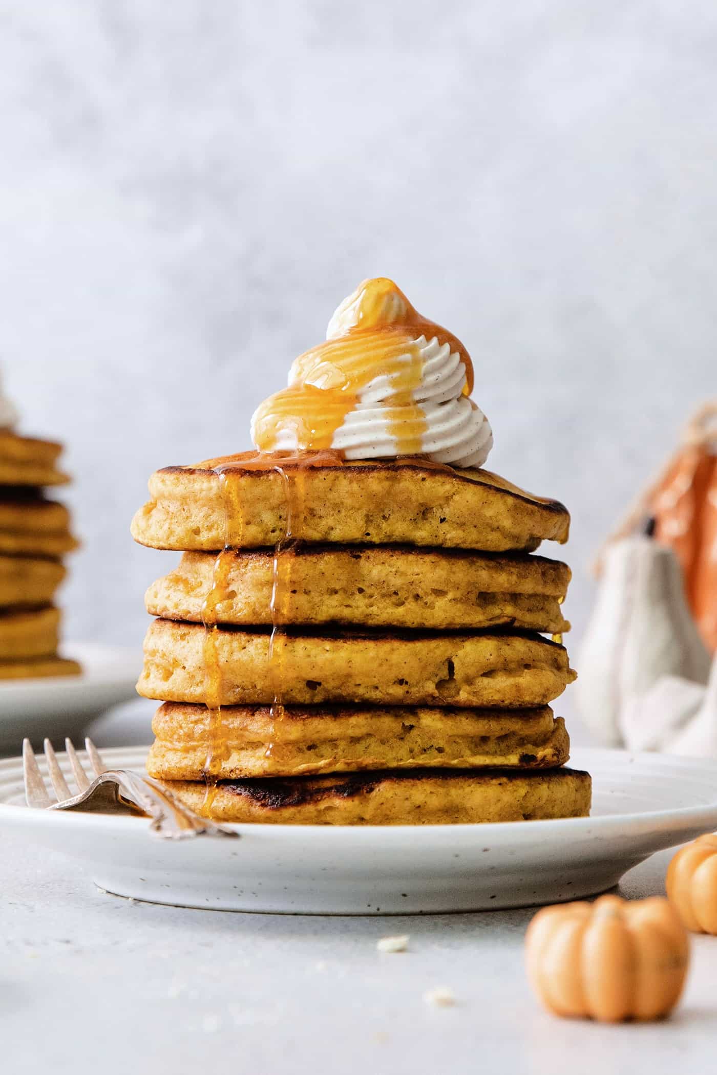 A stack of pumpkin pancakes topped with maple cinnamon whipped cream on a white plate.