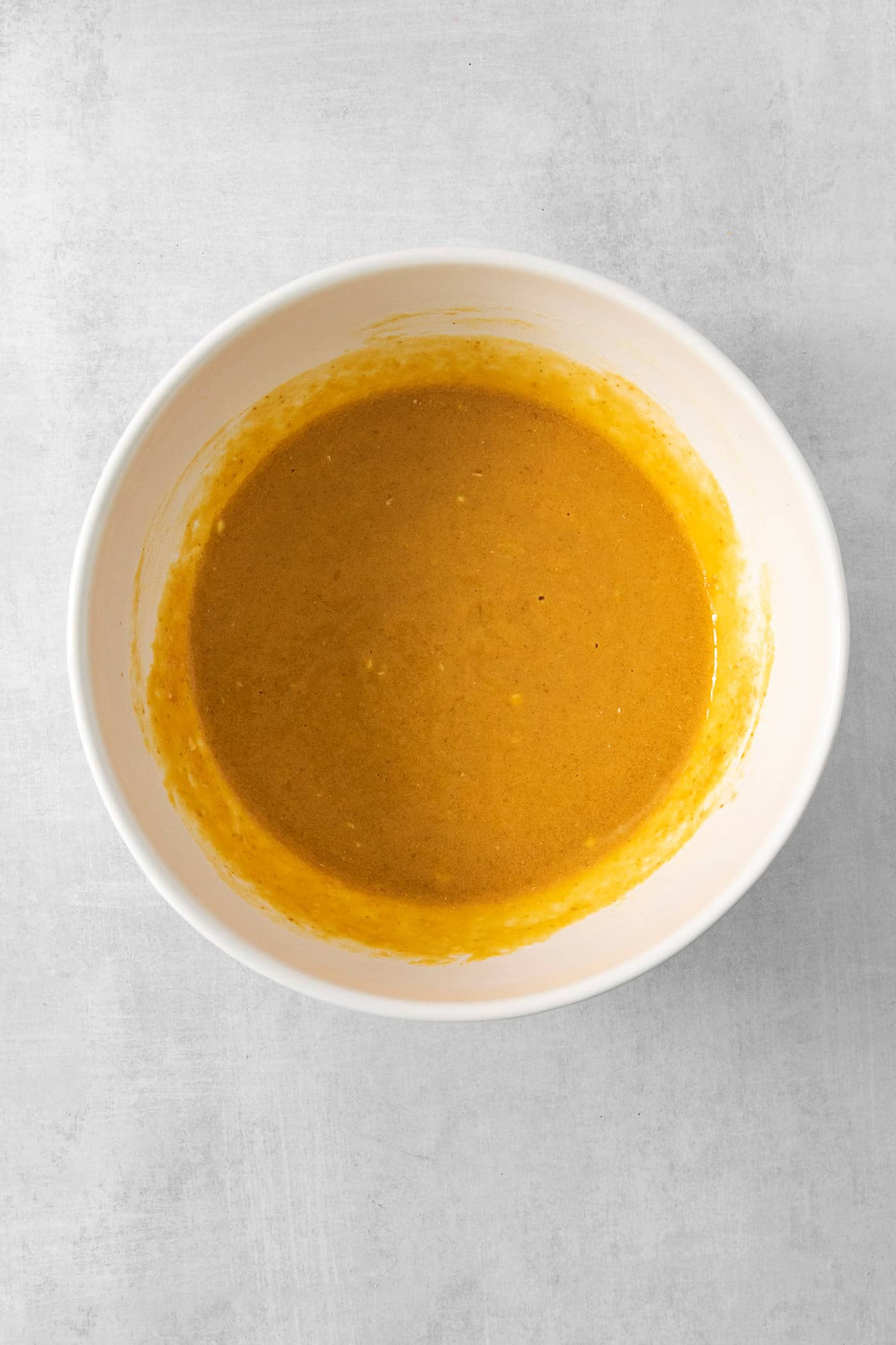 Pumpkin puree is mixed with other ingedients in a white bowl to make pumpkin pancakes.