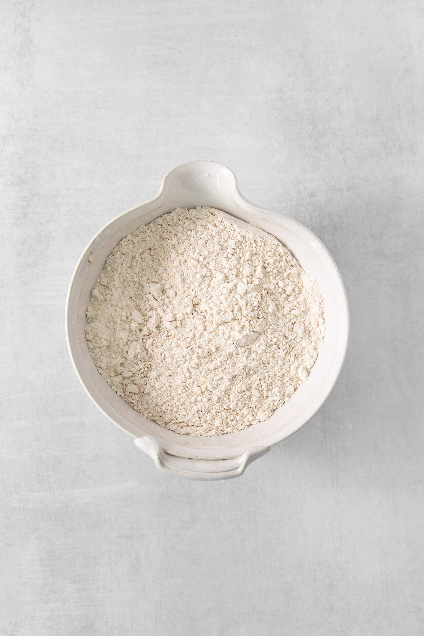 The dry ingredients for pumpkin pancakes are seen in a white bowl on a white background.