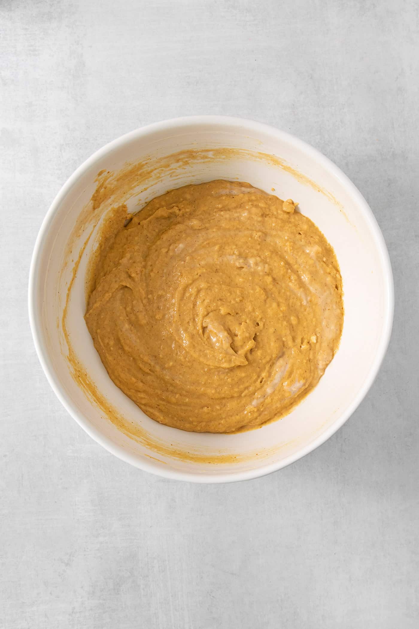 A white bowl full of pumpkin pancakes batter is shown on a white background.