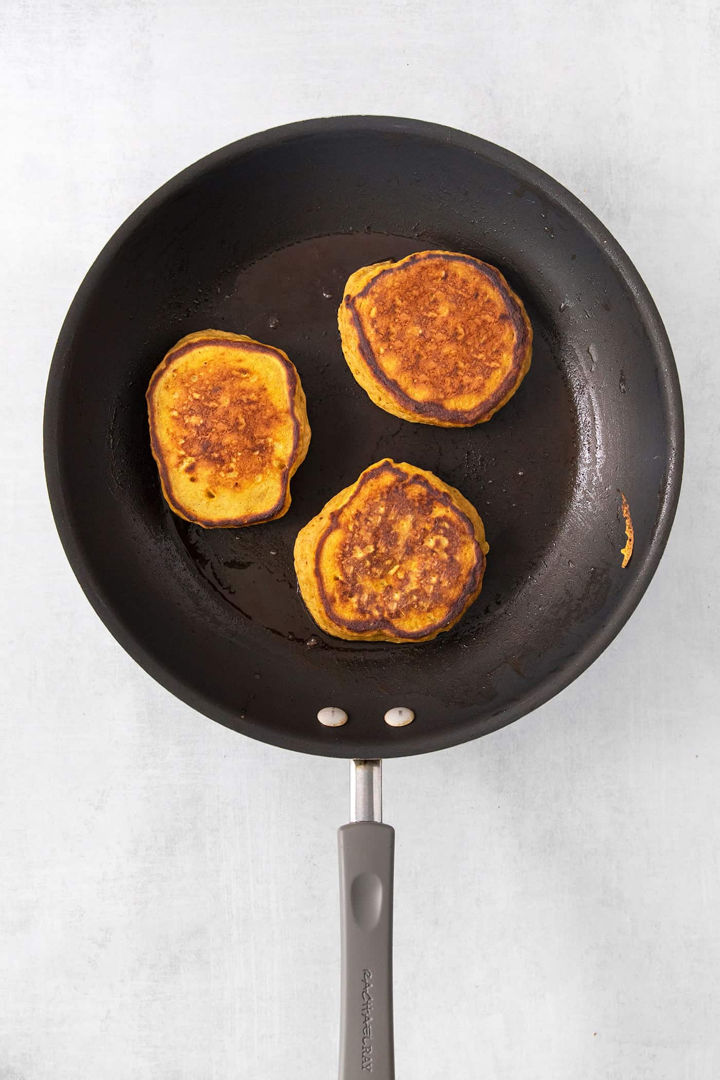 Three pumpkin pancakes cook in a frying pan.