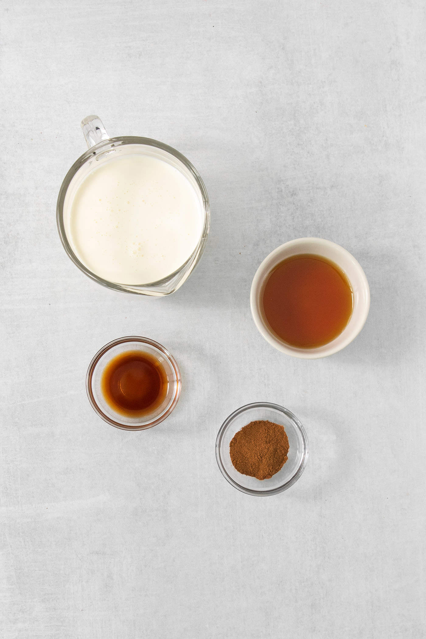 Ingredients for maple cinnamon whipped cream are shown on a white background: cream, maple syrup, cinnamon, and vanilla.