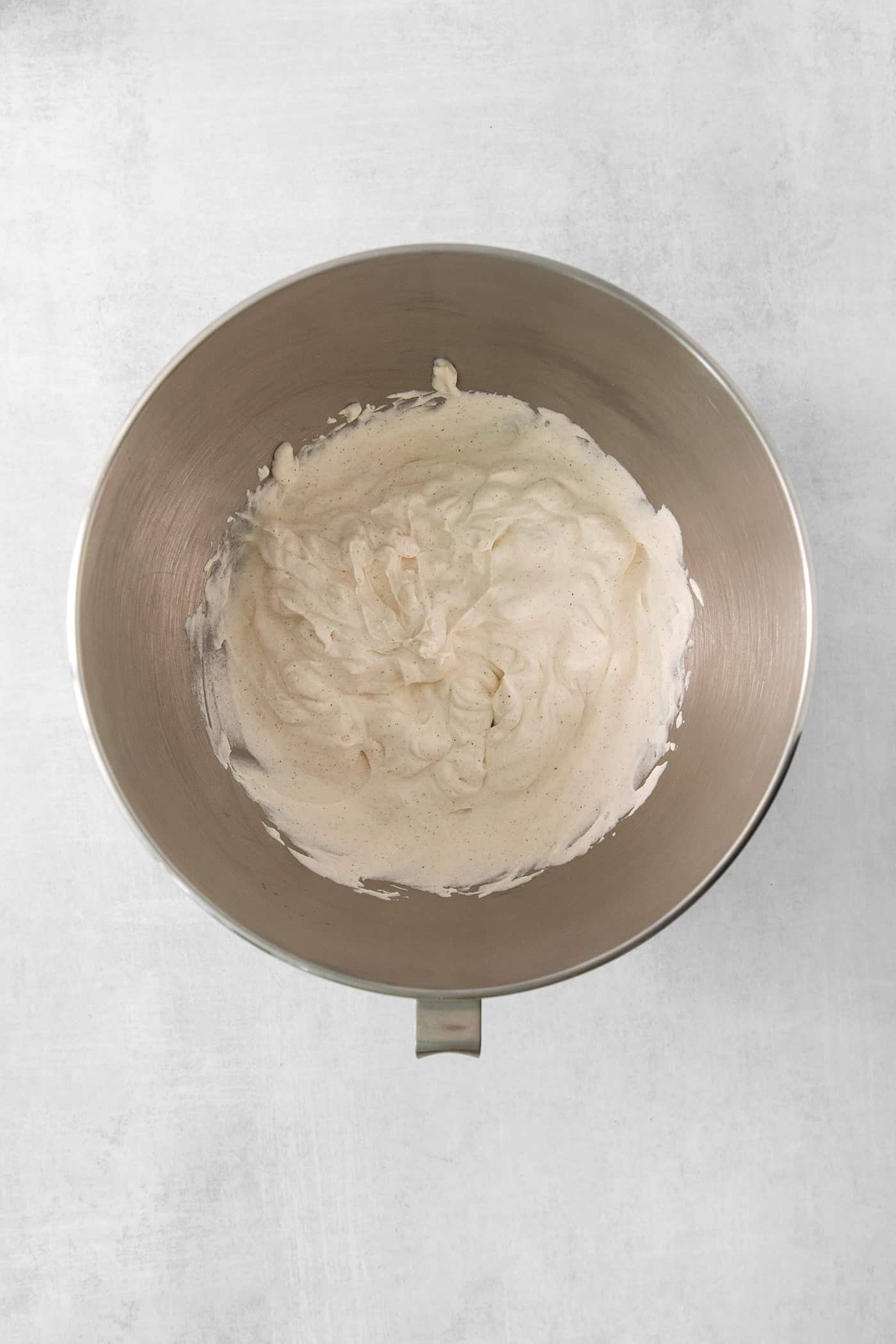 Maple and cinnamon whipped cream is shown in a silver bowl on white background.