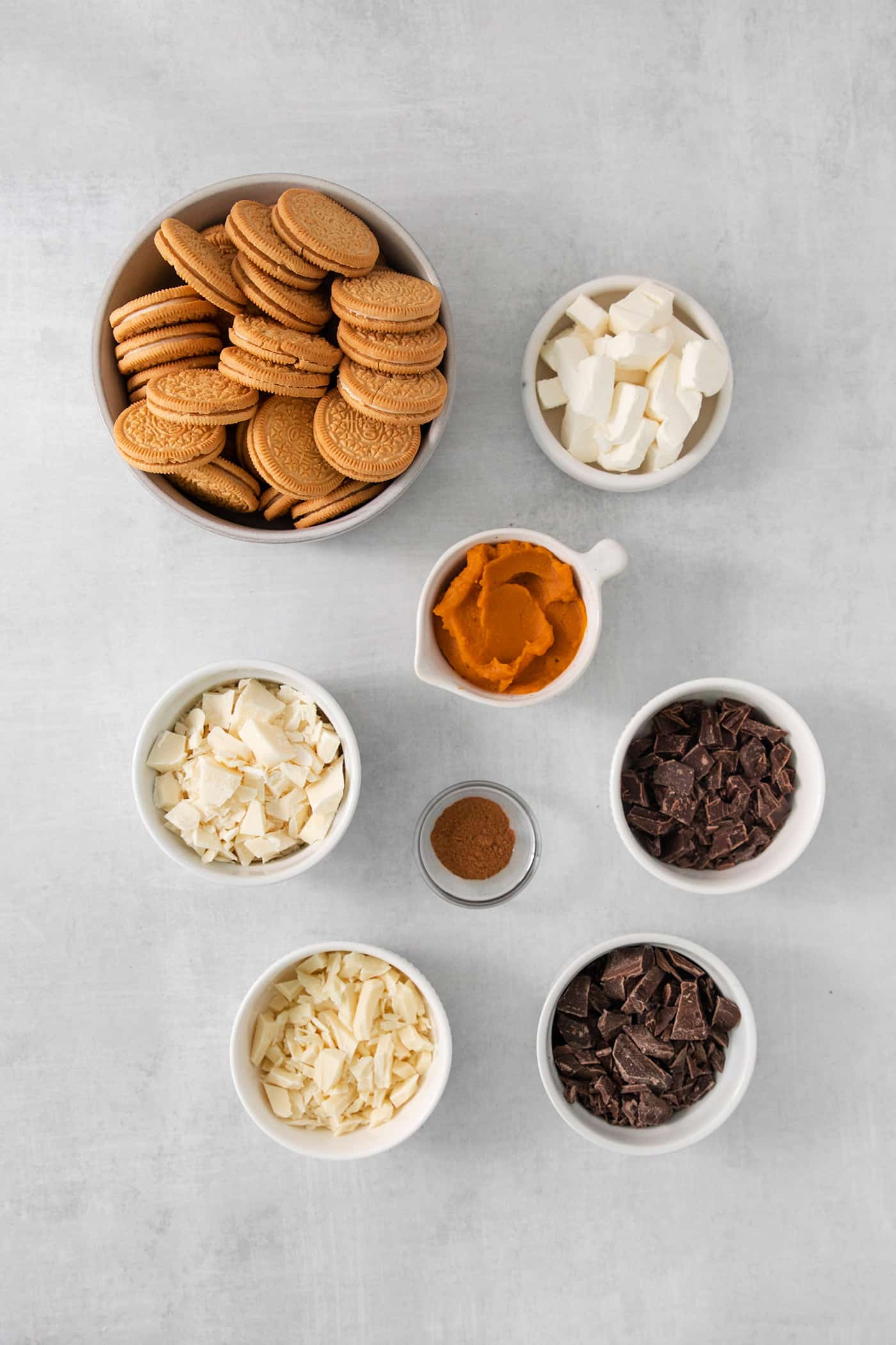 Ingredients for pumpkin pie truffles are shown in bowls: golden Oreos, pumpkin puree, sugar, spices, and cream cheese.