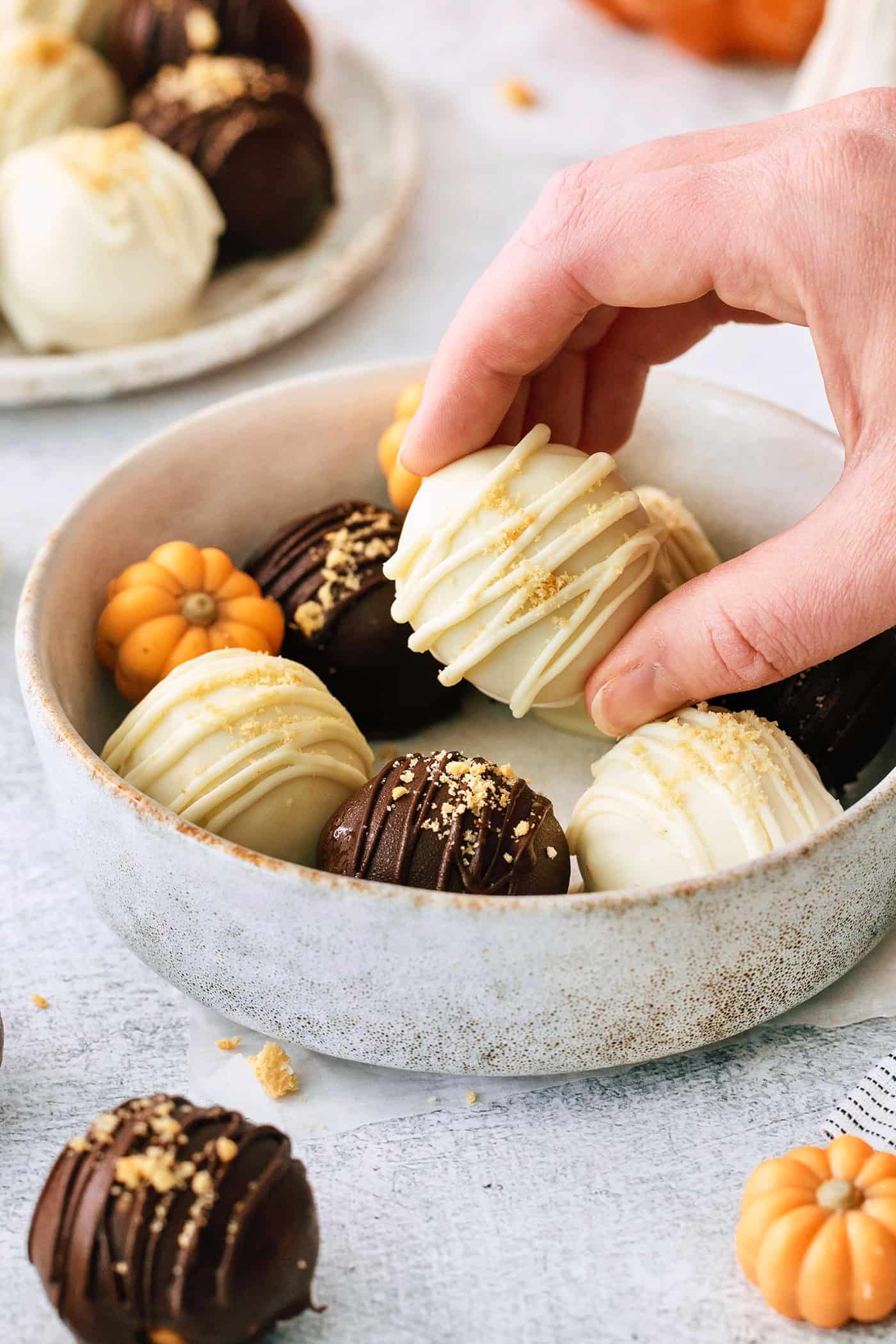 A hand picks up a white chocolate covered pumpkin pie truffle from a bowl of truffles.