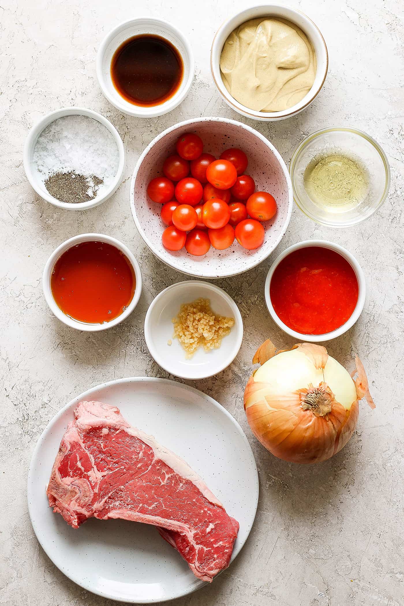 Ingredients for honey mustard beef kabobs are shown in bowls: tomatoes, beef, olive oil, salt and pepper, onion, sriracha.