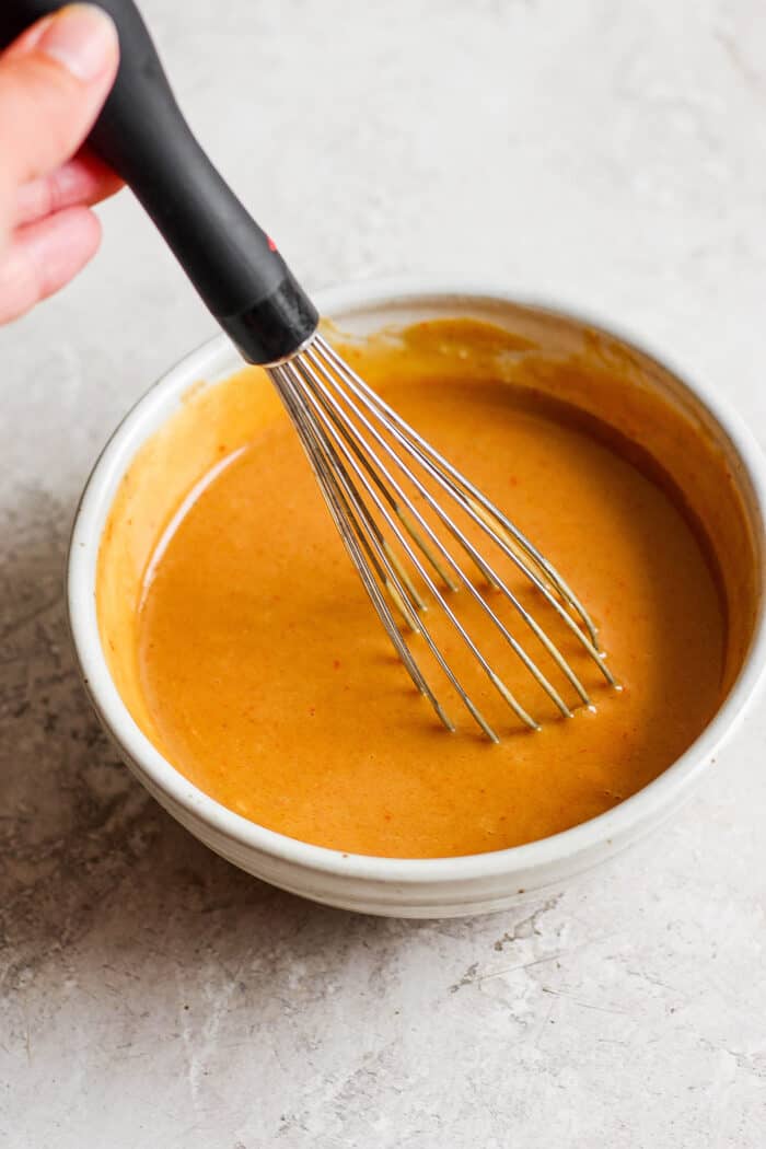 A whisk stirs a white bowl of marinade for honey mustard beef kabobs.