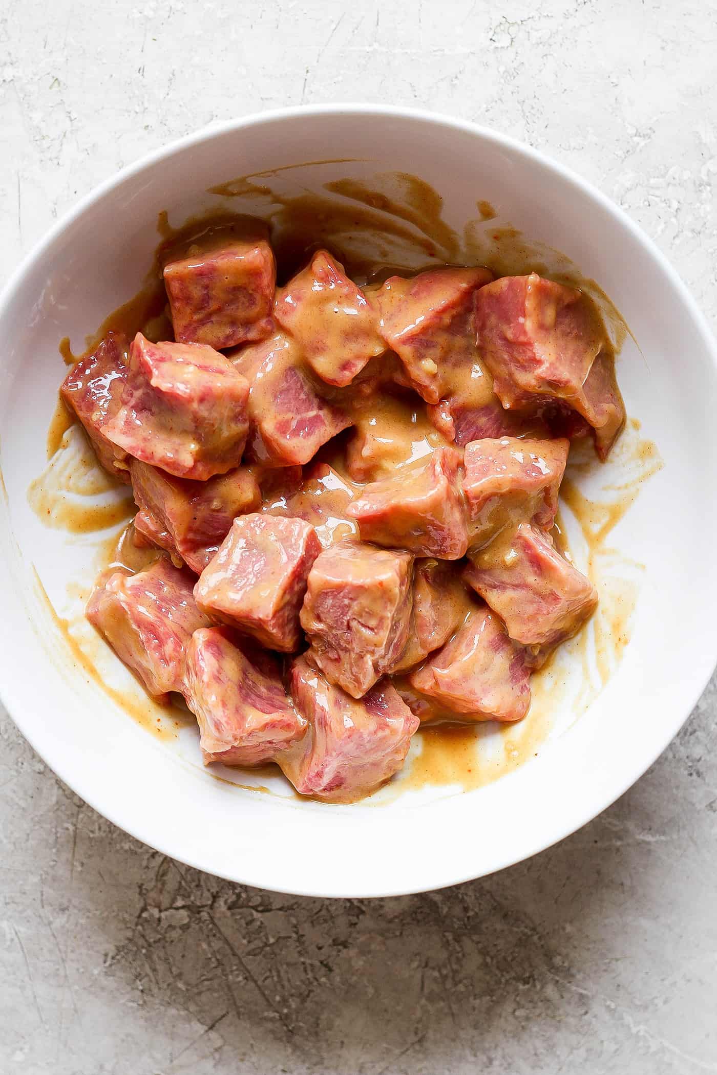 Meat marinates in a white bowl for honey mustard beef kabobs.