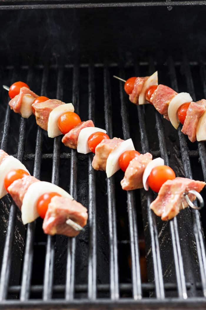 Skewers of honey mustard beef kabobs with vegetables are shown cooking on a grill.
