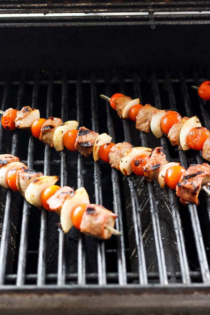 Skewers of honey mustard beef kabobs with vegetables are shown cooking on a grill.