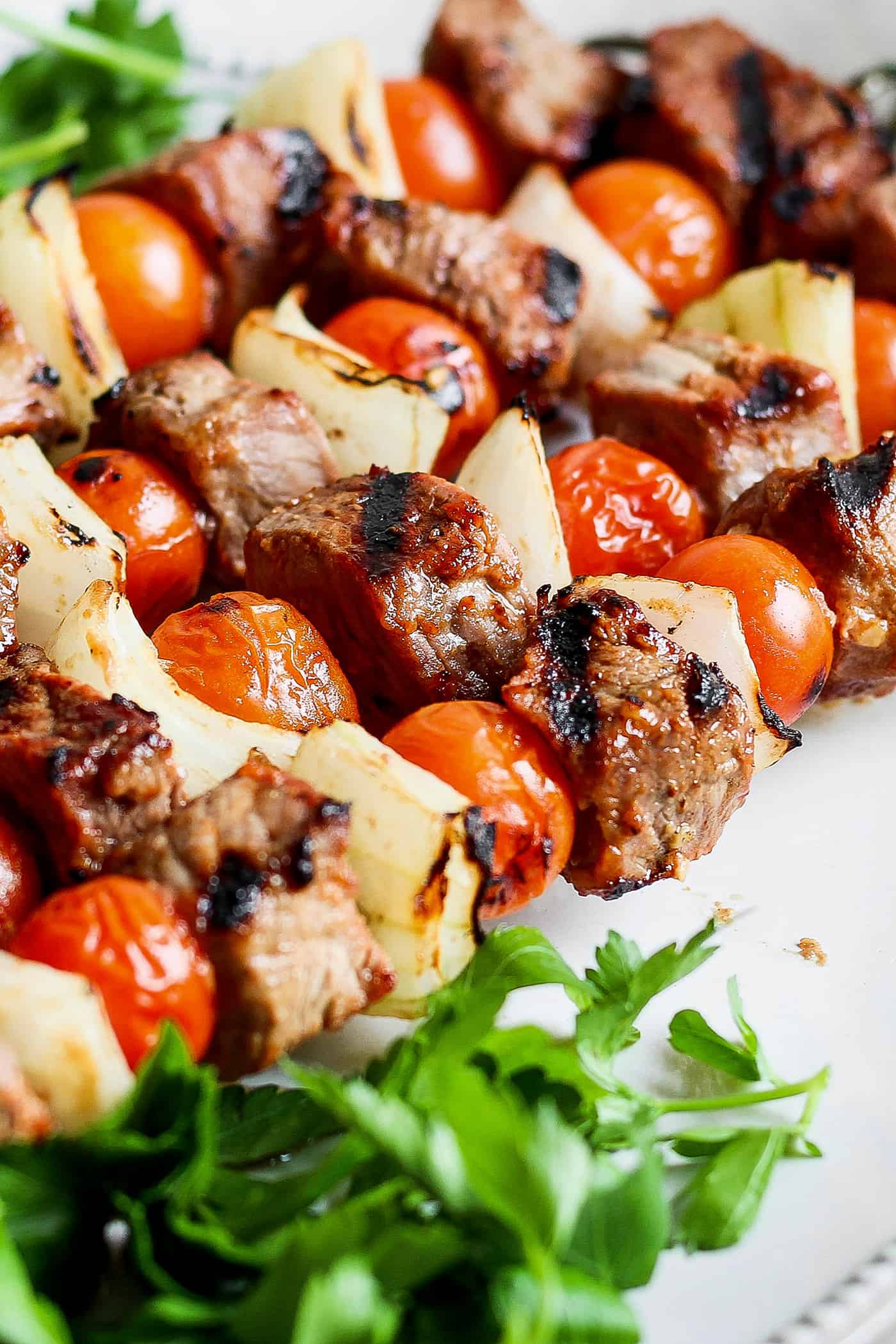 A close up of honey mustard beef kabobs with tomatoes and onion.